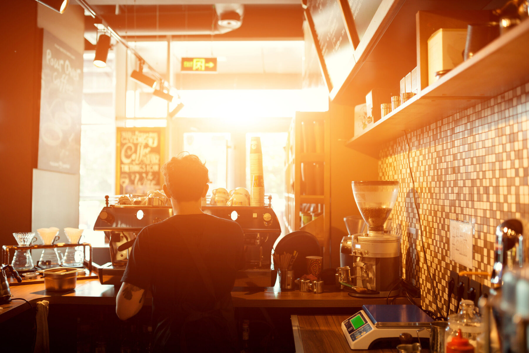 A man stands at the coffee shop counter serving coffee to guests.