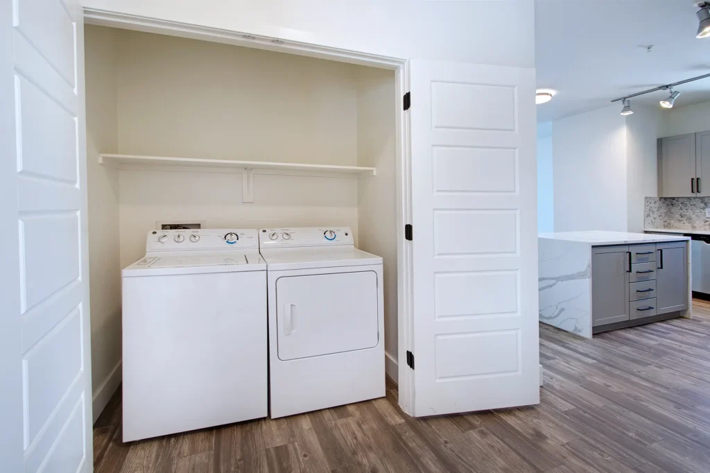 A laundry room featuring a washer and dryer, with shelves and cleaning supplies visible in the background.