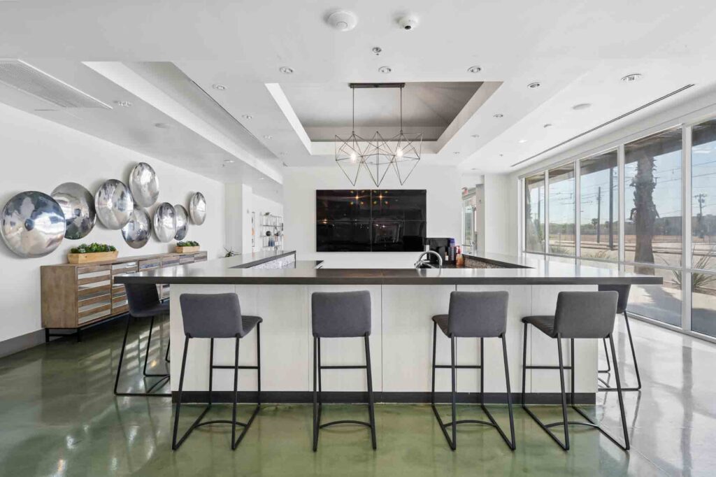 Modern kitchen with a large island, four bar stools, a geometric light fixture, wall art featuring round metallic discs, and floor-to-ceiling windows letting in natural light.